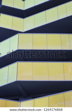 Close up outdoor view of a modern facade made of pattern of reflective glass panels. Abstract design with geometric shapes and angular lines. Bright colored building with yellow and blue tones. 