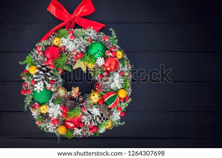 Top view Beautiful hand made traditional bright Christmas wreath decorated with pine cones, spruce branches,berries, balls, stars and decorative beers on black wooden background, flat lay. Copy space