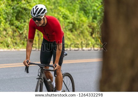 Close up on Asian man who's cycling a road bike up high on hill in the morning.