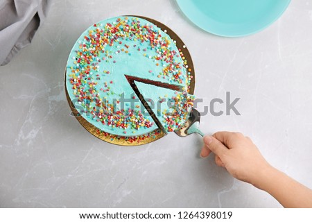 Woman taking slice of fresh delicious birthday cake at table, top view