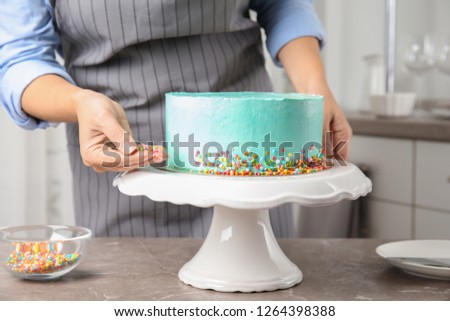 Woman decorating fresh delicious birthday cake in kitchen, closeup