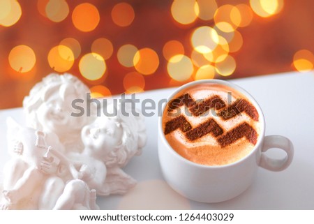 a cup of cappuccino coffee with a pattern of the aquarius zodiac sign on milk foam