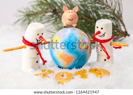 Pink pig on the globe and two snowmen on the background of a fir branch and golden numbers 2019 in the snow in the foreground