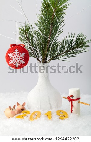 Golden figures lie in the snow against the background of two piglets, a snowman and a white vase with a fir branch