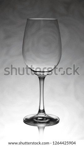 Empty transparent glass wine glass stands on a glass closeup. In the background is a silhouette drawing of flowers
