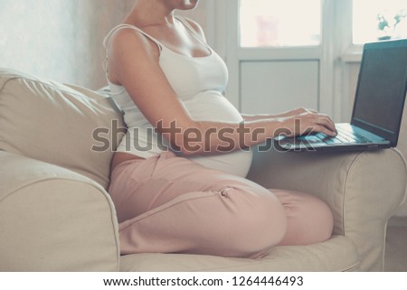 Young beautiful pregnant woman working on laptop. Pregnant business woman searching information and online shopping on laptop prepare for childbirth and parenting on sofa at home. toned