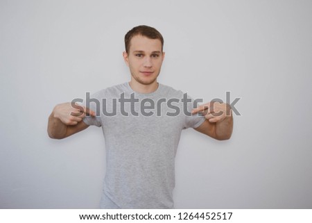 a man in a gray t-shirt shows his shirt with his fingers on a white background, free space