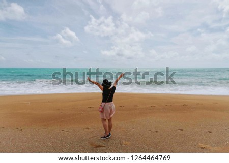 Back side view - Close up of happy traveler woman wearing black hat, t-shirt, pink short & bag raising hands with tropical sea water, waves, golden beach & white clouds blue sky background, copy space