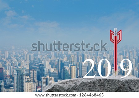 Red pencil in the shape of a dart arrow with 2019 white text on rock mountain over modern city tower, office building and skyscraper, Business strategy happy new year 2019 concept