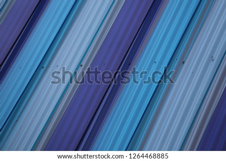 Close up outdoor view of colorful parallel panels of a modern facade. Abstract design with pattern of decorative bands colored in blue and violet. Graphic picture with reflective surfaces.