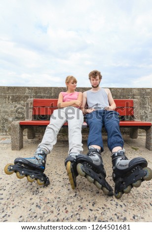 Young people friends in training suit with roller skates. Woman and man relaxing on bench outdoor.