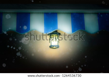 The street lamp shining in the evening under a striped canopy, in the winter under snow