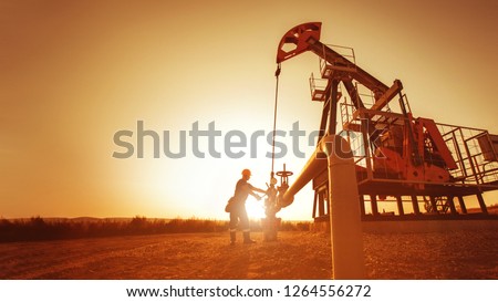 Oil worker is checking the pump near oil derrick on the sunset background.