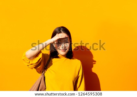 Beauty and fashion woman smiling in orange top with hand on forehead with orange background.