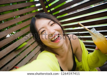 lifestyle portrait of young beautiful and happy Asian American student girl taking selfie portrait photo outdoors drinking orange juice smiling cheerful enjoying holidays trip in sweet face expression