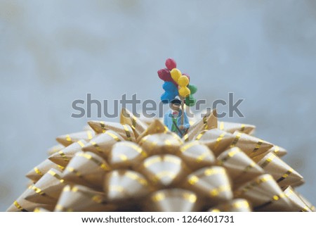 Miniature people: uncle holding with floating balloon stand in golden bow. Merry Christmas and Happy New Year concept.