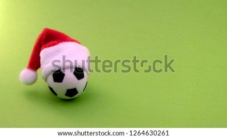 Christmas and football. Ball for playing football with a red Santa Claus hat on a green background. Copy space.
