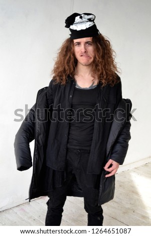 photo portrait of a guy with long curly hair in black clothes fooling around on a white background