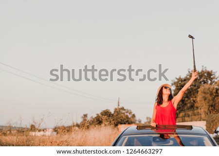 beautiful young woman taking a selfie on top of a the car on a sunny day. Travel and fun concept