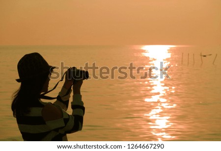 Silhouette of a woman taking pictures at the sun rising seaside