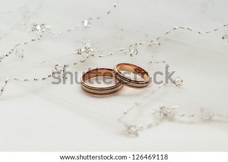 Two wedding rings from yellow and  gold lie on a veil of the bride