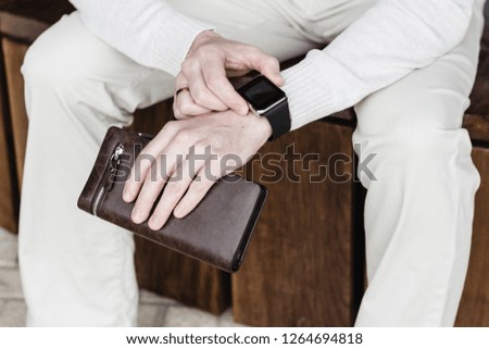 A man sits with a wallet in his hands and using his smart watch app.