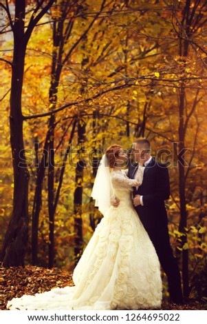 Young wedding romantic couple of bride in white dress and bridegroom in suit standing in autumn deep forest outdoor on natural background, vertical picture