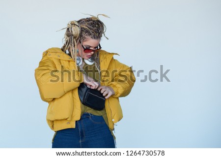 young blonde girl in sunglasses with african pigtails listens to music in headphones and dances against a white background.