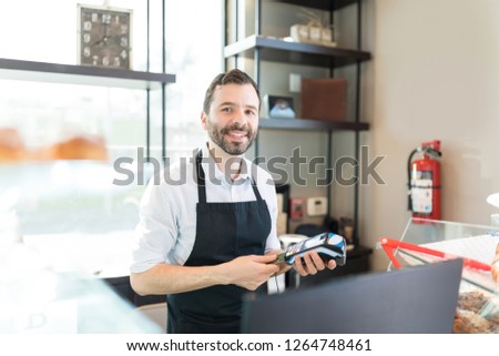 Portrait of mid adult seller receiving payment through credit card at bakery store