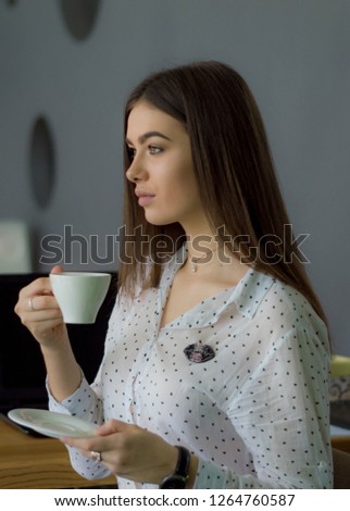 
Young beautiful student in a cafe is drinking a cup of coffee