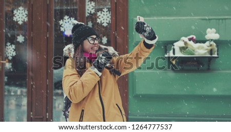 Beutiful Young Girl in the snowy city makes a selfie. Slow motion. Portrait of stylish young beautiful girl in a winter city