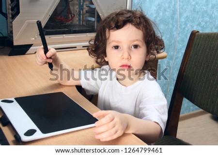 Little 2 3 year old baby girl in white clothers draws at the home computer in graphics drawing tablet. child is holding a pen.