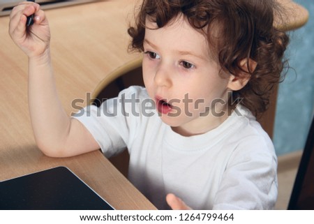 Little 2 3 year old baby girl in white clothers draws at the home computer in graphics drawing tablet. The child is holding a pen. emotion surprise. Close up.