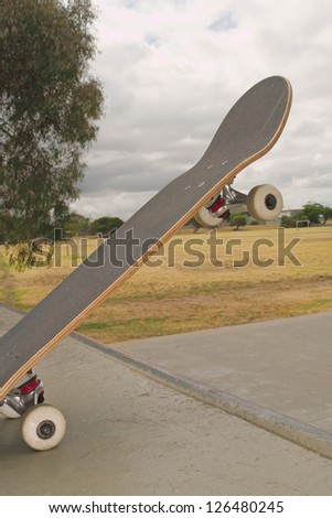 Skateboard lifted over skate ramp edge with two wheels on ground, grass and cloudy sky in background