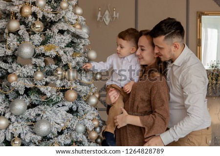 Parents and their little son decorating Christmas tree with toys and garlands.