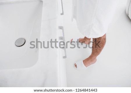Horizontal photo of the man in white bathrobe and white house slippers standing in front of the sink