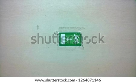 Texture and background, wallpaper of a taped green tattered paper sign indicating a person direction to the exit on the beige-white concrete wall in a public place.