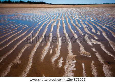 The coastal strip (coastline, beach) at low tide. A desert area with wet sand, a wavy relief runs along it. Sky reflects in the remnant of water. Mackay, Queensland, Australia. Closeup