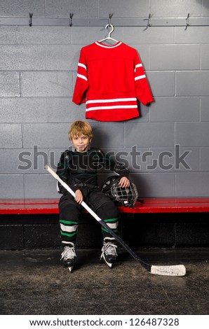 A Young Boy in Dressing Room partially dressed in hockey equipment