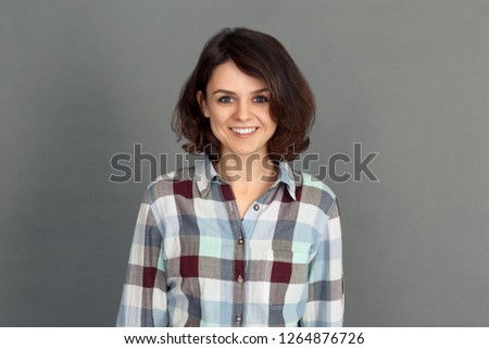 Young woman standing isolated on grey wall looking camera smiling cheerful close-up