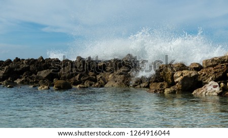Waves crash over rocks sending water into the air. Bright blue summer sky of a tropical island and clear turquoise water. Dramatic coastal scene.