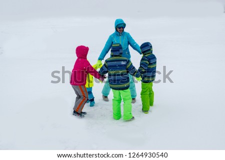 Happy young mother in blue ski suit wearing sunglasses with funny children in bright winter clothes jumping for joy on shore of icy lake. Wonderful winter vacation for whole family. Kids fun together