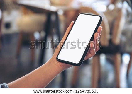 Mockup image of a hand holding black mobile phone with blank white desktop screen in cafe