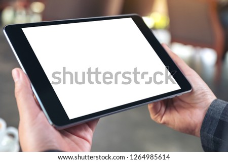 Mockup image of hands holding and using black tablet pc with blank white desktop screen in cafe