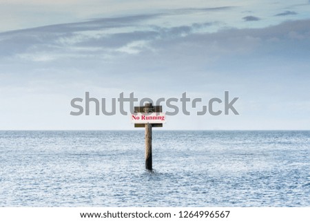 No Running warning sign in red letters on post in ocean.