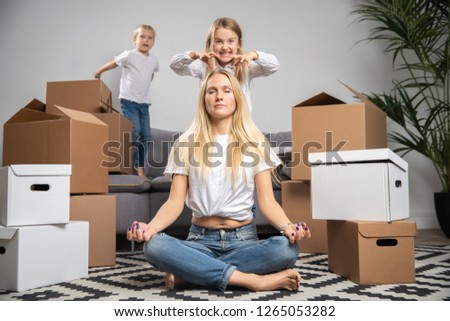 Picture of calm woman sitting on floor among cardboard boxes and boy, girl jumping on sofa