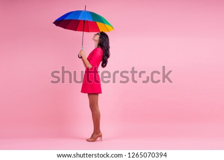beautiful brunette girl in the studio on a pink background in the style dress with rainbow an umbrella