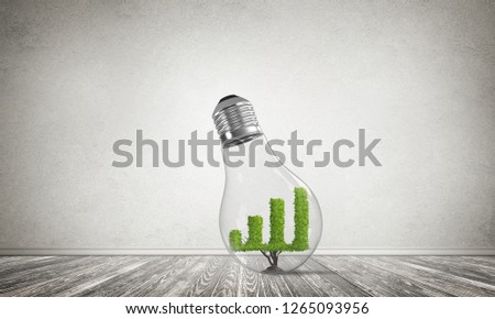 Glass lightbulb with growing green graph inside in empty room with grey wall on background. 3D rendering.