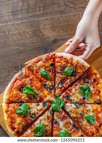 woman Hand takes a slice of sliced Pizza with Mozzarella cheese, Tomatoes, pepper, olive, Spices and Fresh Basil. Italian pizza. Pizza Margherita or Margarita on wooden table background