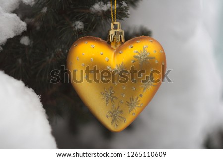 Christmas decoration in the form of a golden heart with patterns on the background of snow-covered coniferous tree close-up
